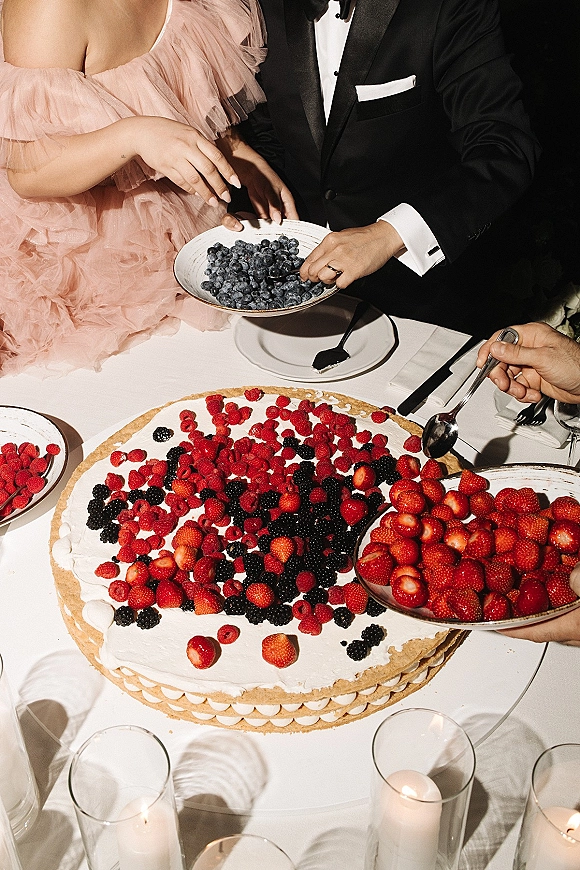 Wedding dessert table with a berry wedding dessert giant tart topped with mixed berries and whipped cream, candlelit reception setting with guests serving