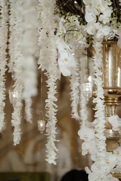 Hanging wedding florals with orchid hanging installation of cascading white orchids and candlelit glass votives against a warm neutral wall