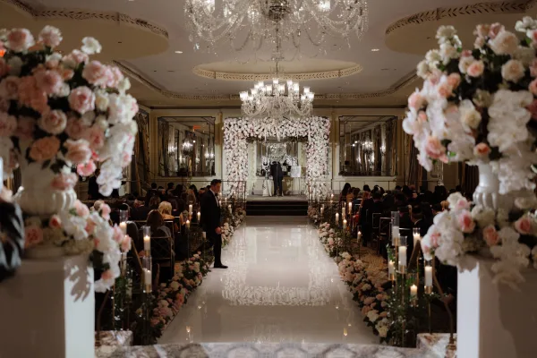 Indoor ceremony setup with a floral arch framing the altar, candlelit aisle runner, and guests seated in a mirrored ballroom