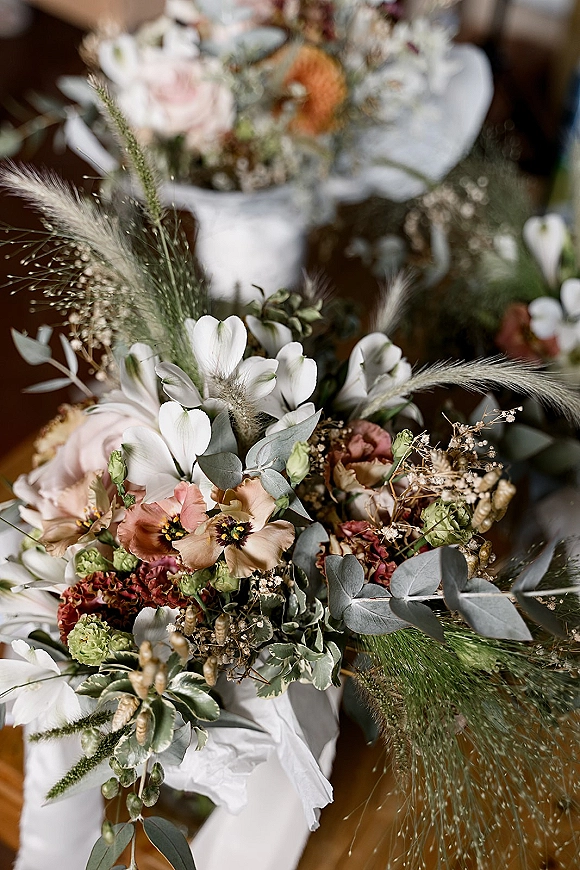 Bridal bouquet with white anemone bouquet and blush roses, pampas grass, eucalyptus, and baby's breath tied with a ribbon in an indoor room