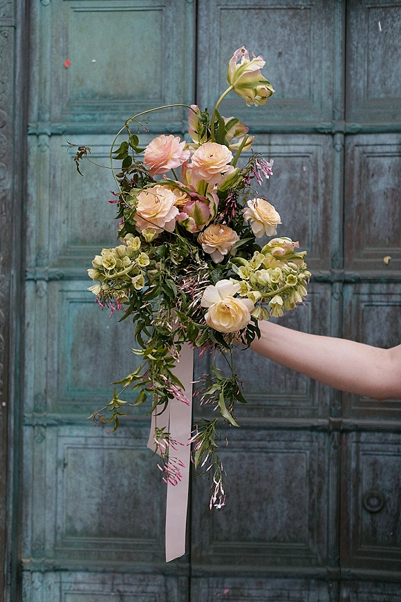 Bridal bouquet of garden roses with airy greenery and trailing foliage tied with a pink ribbon against a weathered blue door backdrop