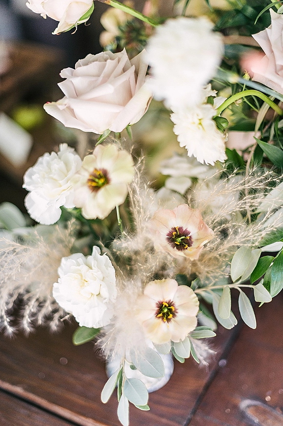 Wedding bouquet of blush and ivory flowers with eucalyptus foliage, featuring pale blush roses and airy pampas grass on a wood table