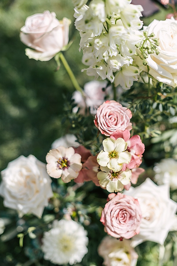 Wedding flowers in blush and white wedding flowers tones, featuring roses and delicate stems with greenery against a garden backdrop