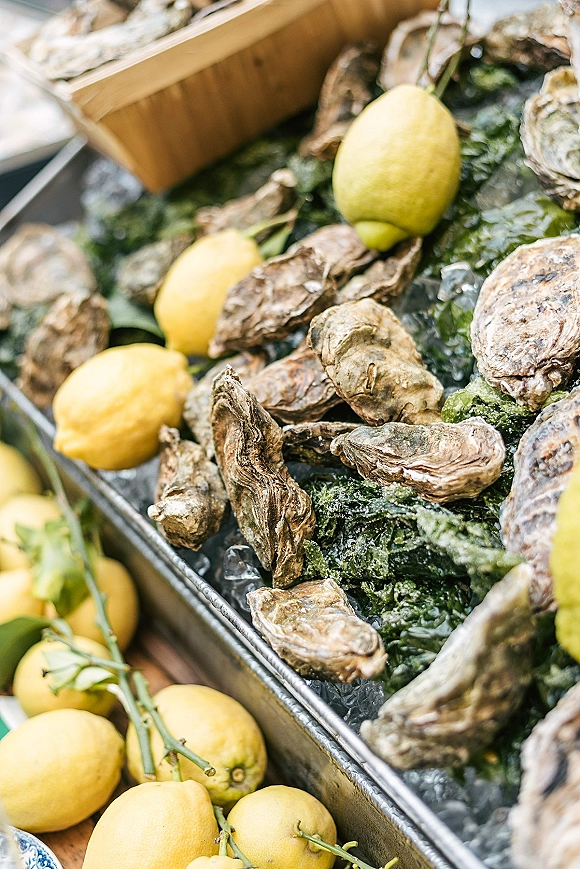 Oyster bar wedding oyster bar display with oysters on ice, lemon wedges, and seaweed on a metal tray atop a rustic wooden crate tabletop