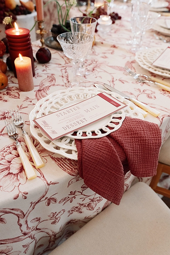Reception tablescape with wedding place setting, lace charger plate, menu card, candles, crystal stemware, and fruit-floral centerpiece on banquet table