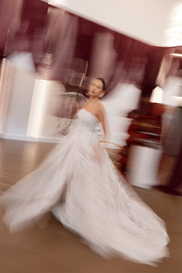 Bridal portrait of a bride twirling in a strapless wedding dress with lace bodice and flowing tulle skirt in a room with burgundy curtains