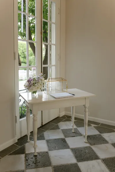 Guest book table with wedding welcome table details, featuring a guest book and pen, hydrangeas in a glass vase, and a gold card box by French doors.