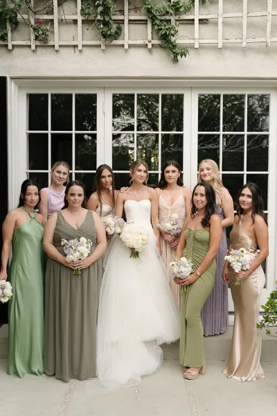 Bridesmaids photo of the bride with bridesmaids holding white and lavender bouquets in mismatched dresses by glass French doors outdoors