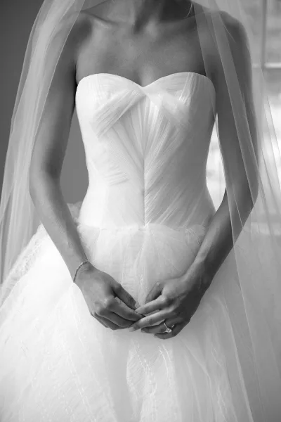 Wedding dress close-up of a strapless gown with ruched bodice and bride’s hands showing an engagement ring in soft window light