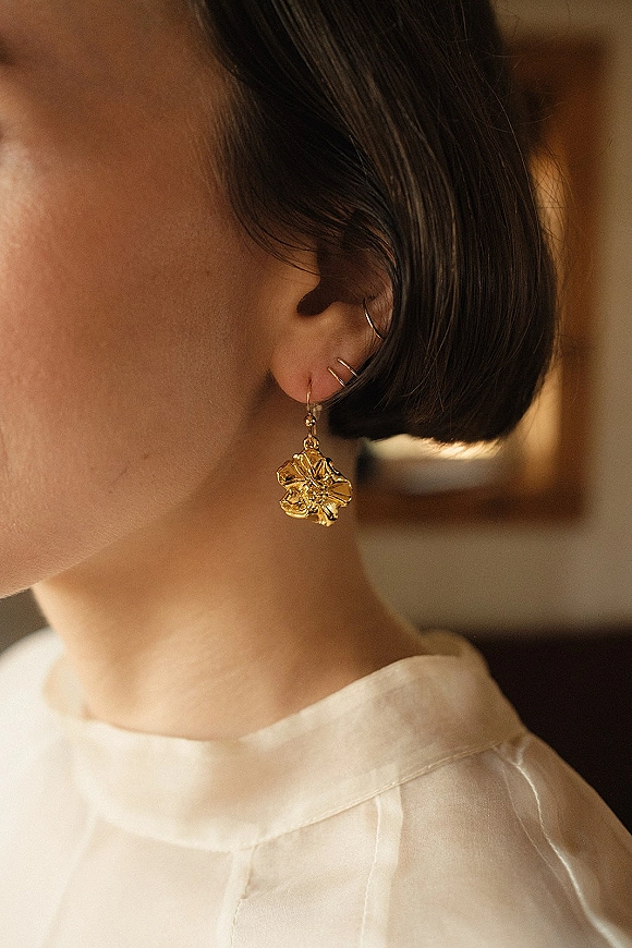 Bridal earrings with gold bridal earrings and a flower charm drop, paired with an ear cuff on multiple piercings, in warm indoor light