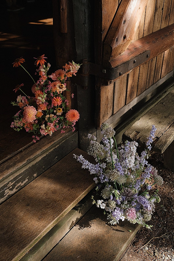 Wedding flowers and wildflower wedding flowers arranged in blush pink, orange, and lavender clusters on rustic wooden barn steps
