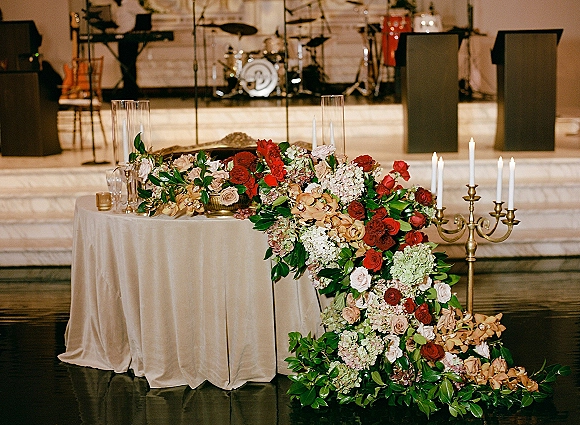 Wedding sweetheart table with sweetheart table florals, cascading roses, hydrangea, orchids, and taper candles on a reception stage with drums behind