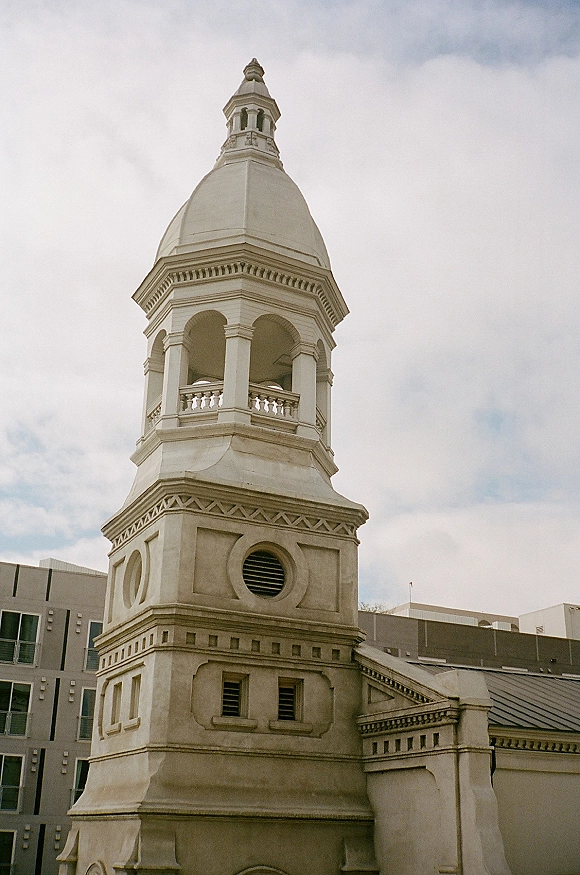 Church steeple wedding church exterior with a domed cupola, arched openings, and balustrade rising above a rooftop under cloudy sky