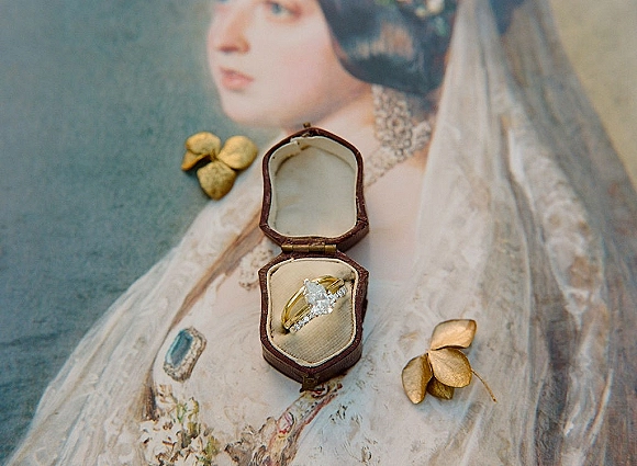 Wedding rings displayed as an engagement ring set in a vintage ring box on a book page with gold leaf accents over a soft blue surface