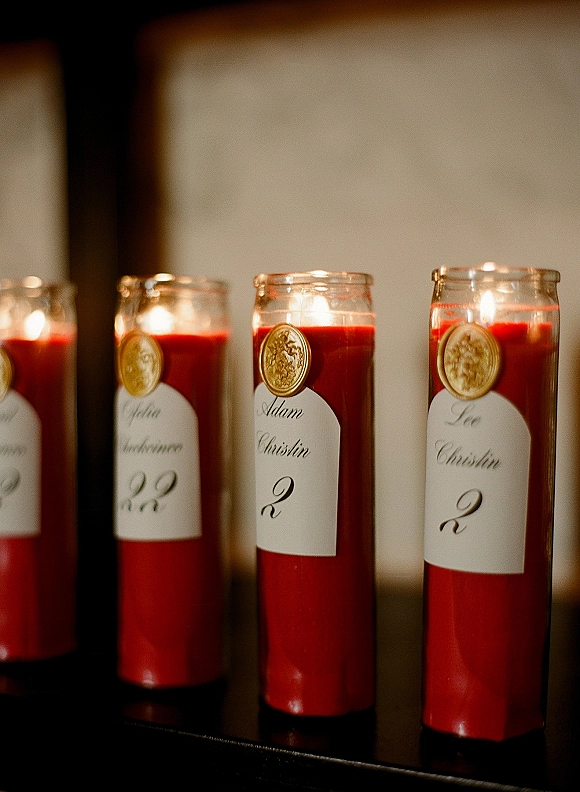 Wedding escort candles with candle escort cards, red wax in glass jars and custom name labels on a tabletop against an indoor wall