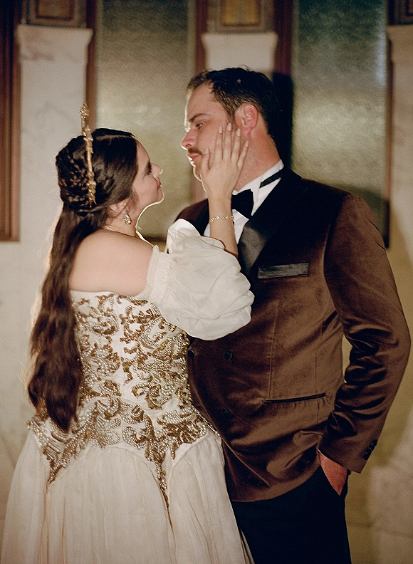 Couple portrait of bride touching groom’s face, forehead to forehead, in beaded puff-sleeve gown and velvet tuxedo by columns indoors