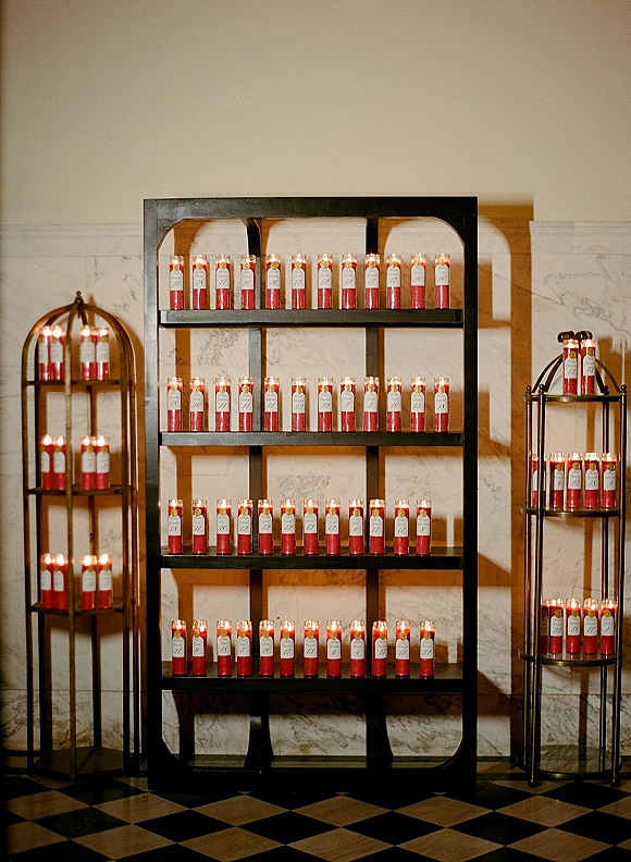 Wedding candle display with prayer candle wedding decor on black metal shelves, red and white glass candles against a marble hallway wall