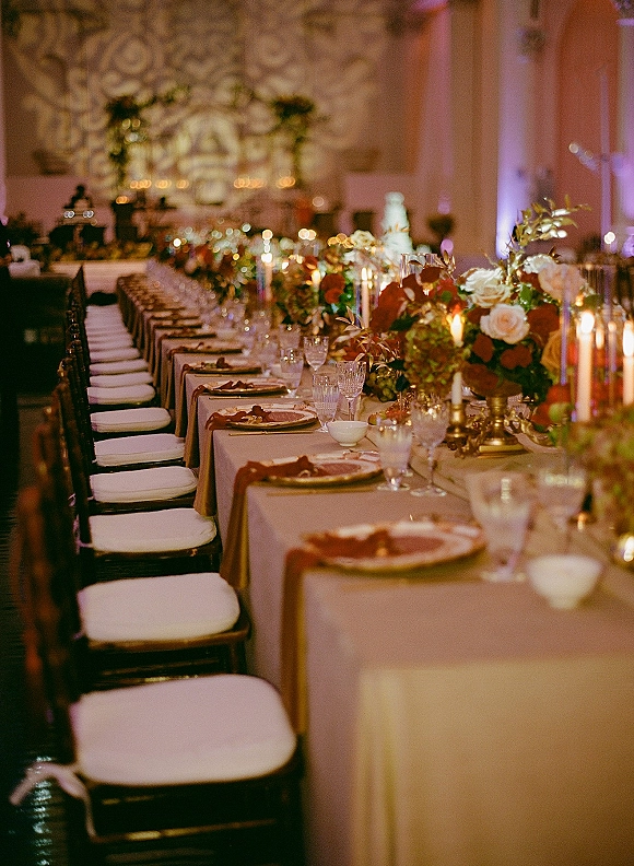 Reception tablescape with a long banquet table, greenery garland and taper candles, formal place settings in a softly lit ballroom