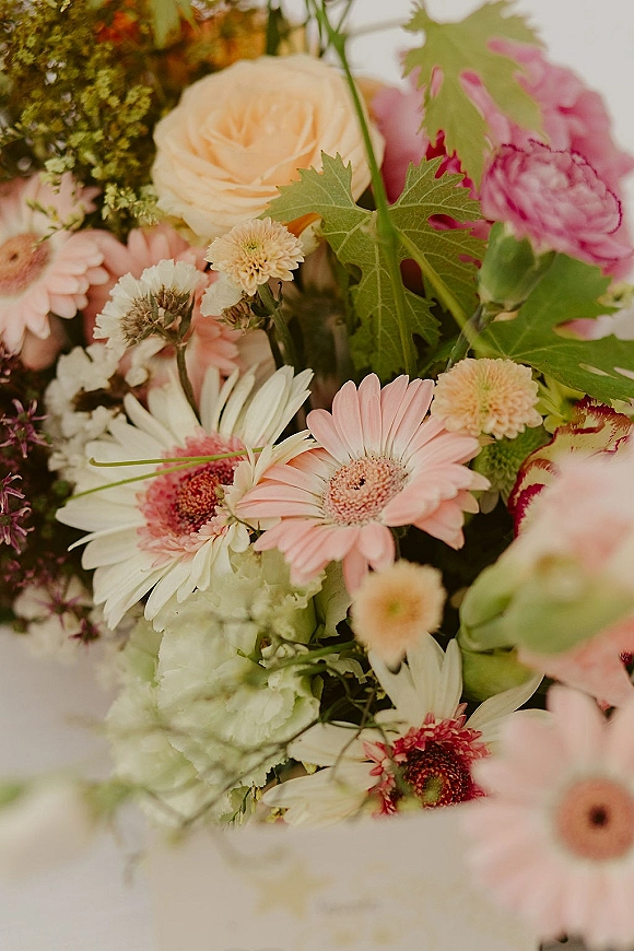 Wedding bouquet with pink wedding bouquet tones, featuring gerbera daisies, ranunculus, and greenery against softly blurred flowers