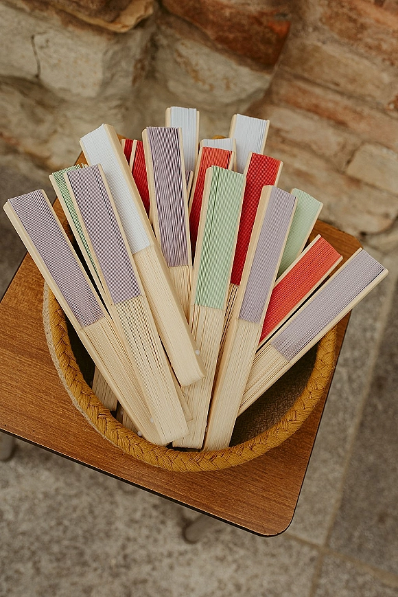 Wedding ceremony fans in a woven basket with wooden handles on a wooden stand against a stone wall and floor