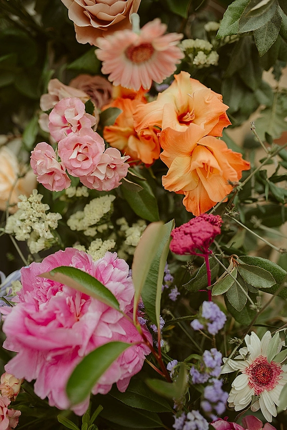 Bridal bouquet featuring a colorful wedding bouquet of roses, peony, gerbera daisies, and baby’s breath against soft-focus greenery backdrop