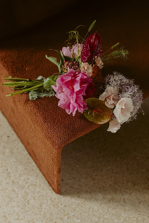 Bouquet close-up with colorful wedding bouquet featuring pink peony, white rose and anthurium, resting on a terracotta velvet cushion