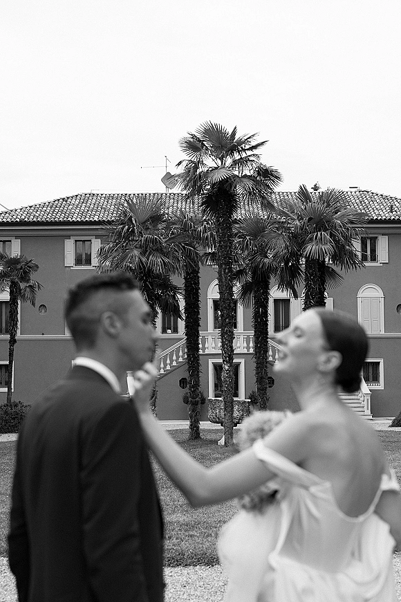 Couple portrait in black and white wedding portrait style, bride laughing while touching groom’s face, villa and palm trees behind