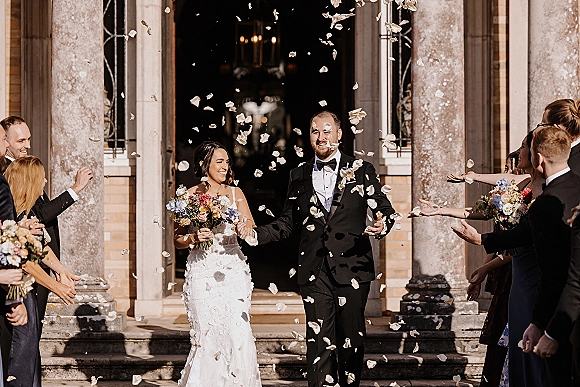 Wedding recessional as bride and groom walk out for a rose petal exit, hand in hand on stone steps, bride holding a colorful bouquet