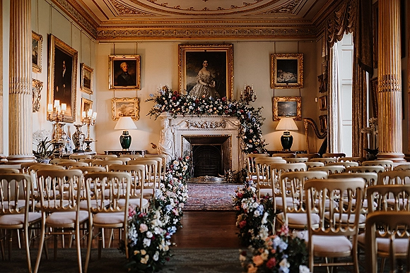Indoor ceremony setup with ceremony aisle flowers lining a greenery runner, leading to a fireplace altar in an ornate mansion room