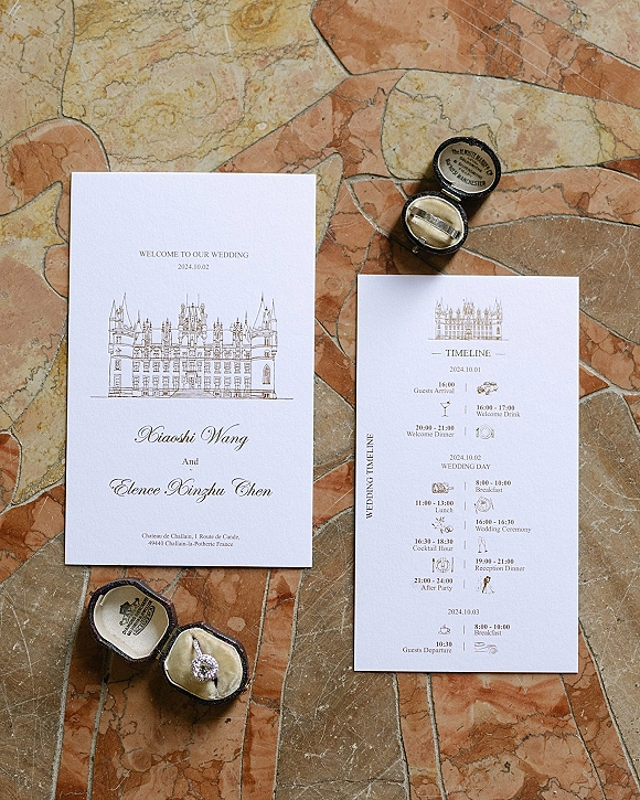 Wedding invitation suite with wedding timeline card, calligraphy and venue illustration, paired with engagement ring in box on stone tile floor