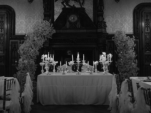 Sweetheart table decor with candelabras and tall taper candles, lush florals, and white linens set before an ornate fireplace mantel backdrop