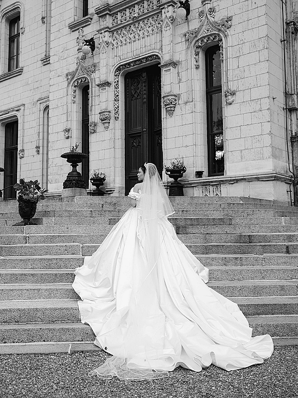Bridal portrait in black and white of a bride on steps wearing a tiara and cathedral veil with a long train by an ornate doorway