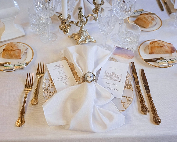 Reception tablescape with formal wedding place setting featuring gold flatware, gold-rim plates, crystal goblets, and silver candelabra with taper candles