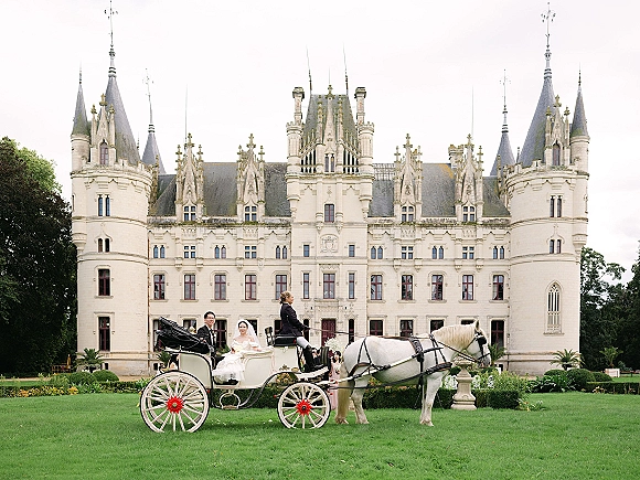 Couple portrait in a horse drawn carriage wedding, bride in a veil and groom in suit, with a castle garden lawn behind them