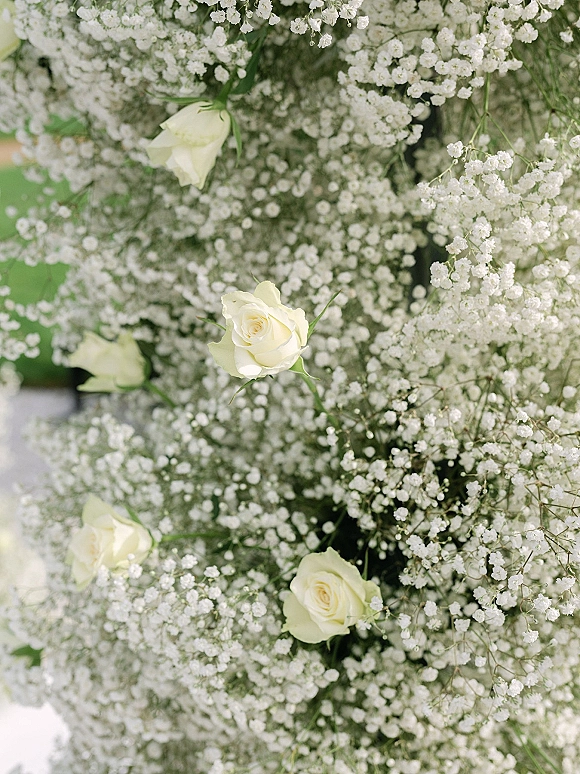 Wedding floral arrangement of white roses and baby's breath with airy greenery stems against a softly blurred greenery background