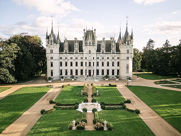 Wedding venue exterior with a castle wedding venue facade, manicured hedges and statues along gravel paths leading to a fountain courtyard