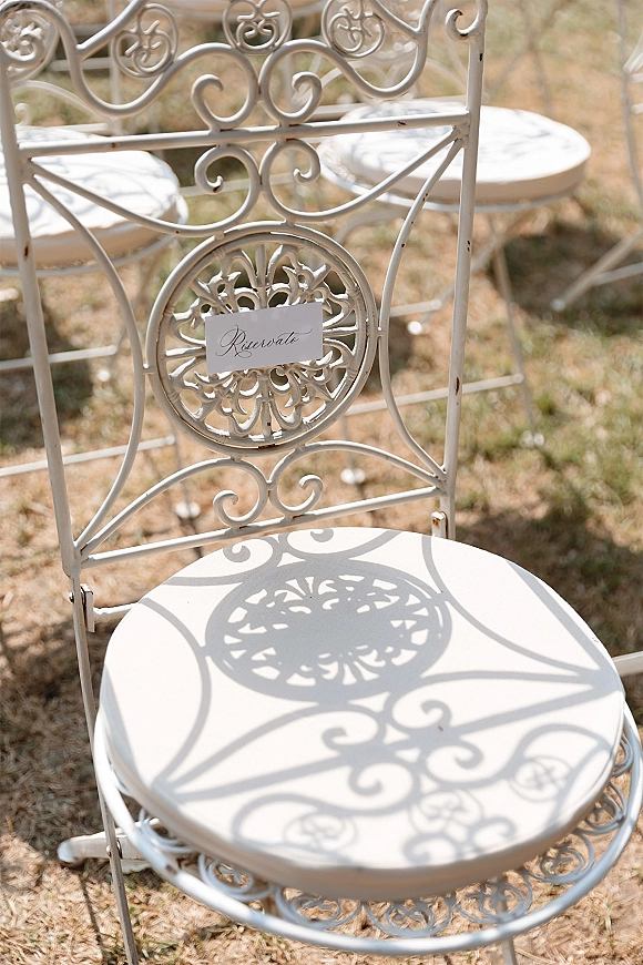 Wedding chair sign with a reserved wedding chair card clipped to a wrought iron chair in sunlight on grass with more chairs behind