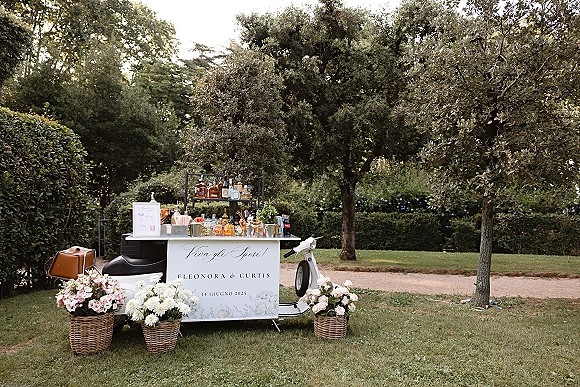 Wedding bar setup with a mobile wedding bar scooter cart, liquor bottles and cocktail glasses arranged on a garden gravel path