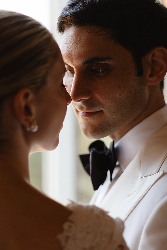 Wedding couple portrait in a close up wedding portrait, forehead to forehead under soft window light, groom in white tuxedo and black bow tie