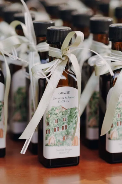 Wedding favors of olive oil wedding favors in glass bottles with custom labels and ribbon bows, grouped together on a wood table