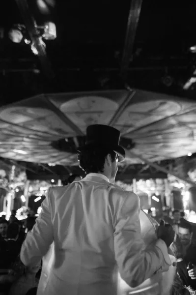Wedding reception moment on the reception dance floor as a guest in a top hat stands among guests beneath bright overhead lighting.