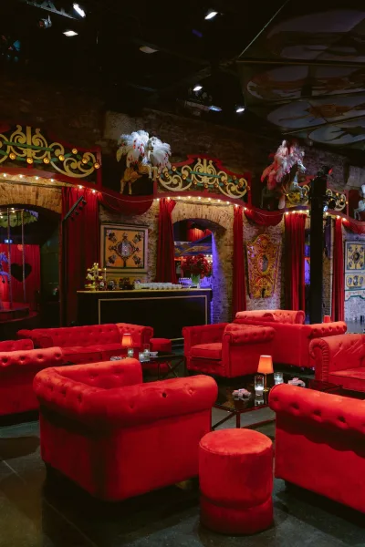 Reception lounge styled for a cocktail hour lounge, featuring velvet sofas amid exposed brick walls and arched doorways under a dark ceiling.