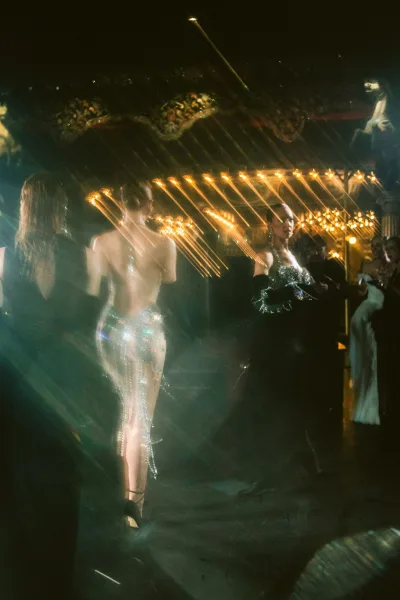 Reception dance floor swirls with wedding reception guests, a sequin dress catching light beneath an ornate ballroom ceiling and stage backdrop.