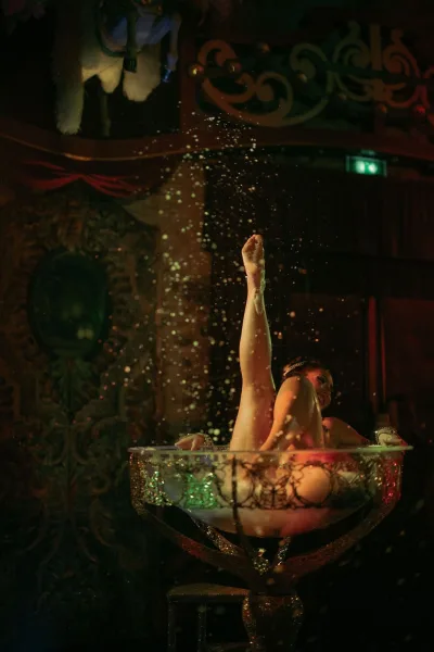 Reception entertainment features a burlesque performance in a giant champagne glass prop on a theater stage with velvet curtain.