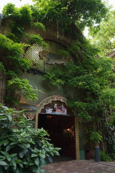 Garden venue entrance with an ivy covered doorway along a brick walkway, set against a stone wall with shrubs and garden trees.