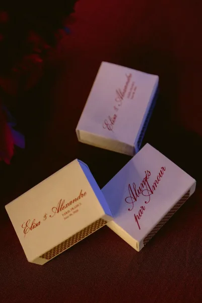 Matchbox wedding favors and custom matchbooks with elegant calligraphy names, styled on rich red table linen for a refined reception detail.