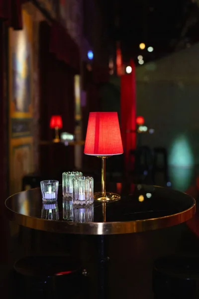 Cocktail table decor on a cocktail hour table with a red lampshade casting warm light against red curtains in a dark lounge.