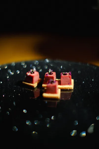 Wedding appetizers arranged as bite size canapés on a glossy black plate, each topped with edible flowers against a dark backdrop.