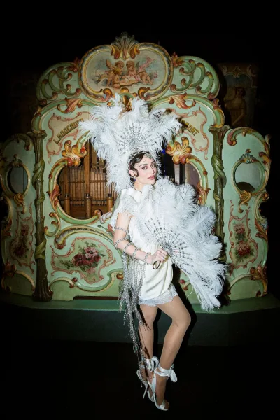 Wedding entertainment as a showgirl wedding performance in a feather headdress, set before a vintage organ facade with painted cherubs.