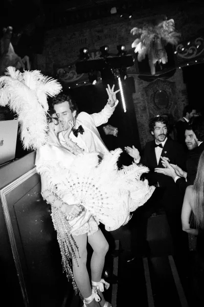 Dance floor moment at a wedding after-party as the couple dances, a feather fan flashing under nightclub stage lights and a cheering crowd.